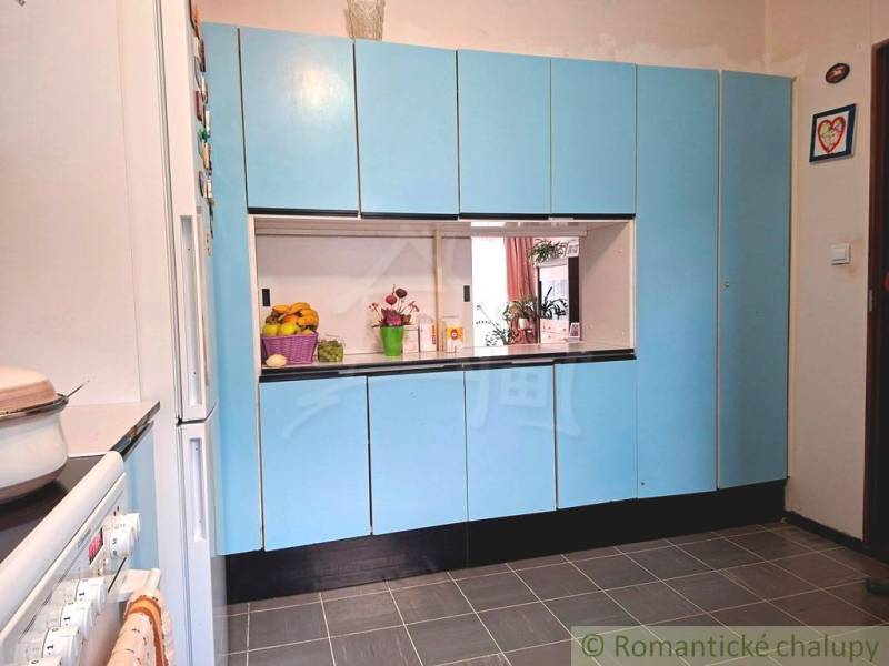 Veľkorysý 10-árový pozemok, slnečná nehnuteľnosť, priestranné bývanie  - Kuchyňa v rodinnom dome s modrými skrinkami a bielymi spotrebičmi.