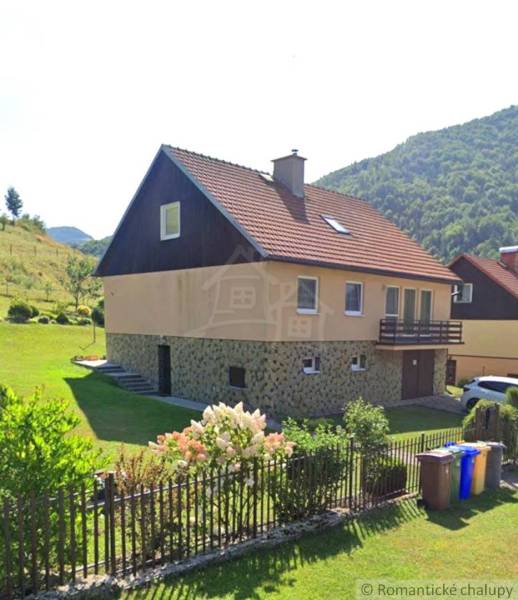 Veľkorysý 10-árový pozemok, slnečná nehnuteľnosť, priestranné bývanie  - Rodinný dom v Liptovských Revúcach s červenou strechou, záhradou a kvetinovým plotom.