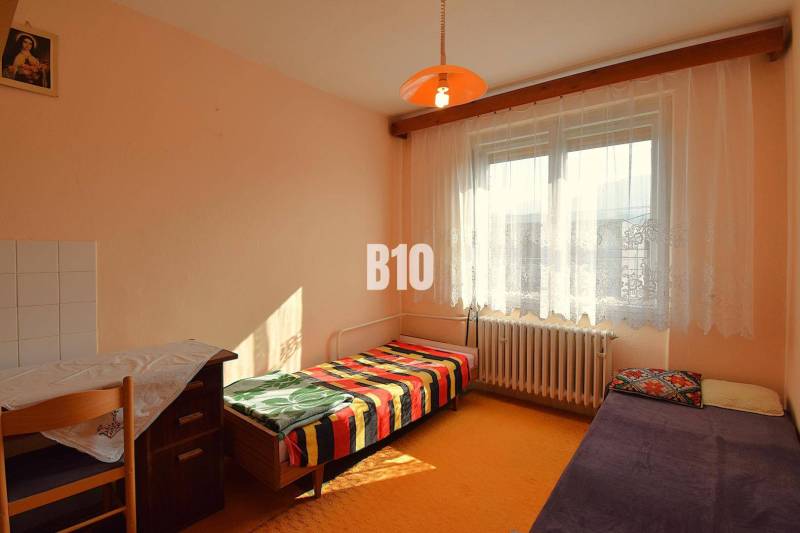 5 izbový  rodinný dom vo Varíne - Izba v rodinnom dome s jednoduchým nábytkom, posteľou a oranžovým lampášom.