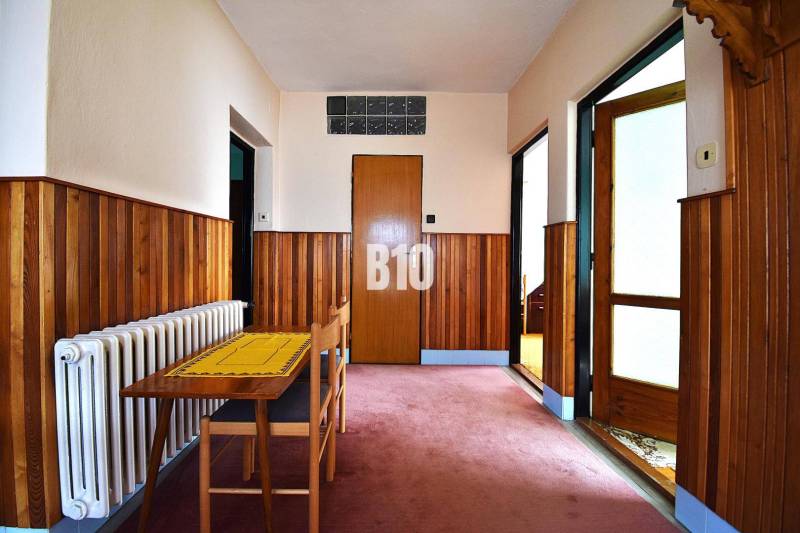 5 izbový  rodinný dom vo Varíne - Chodba v rodinnom dome s dreveným obkladom, stolom a stoličkou.