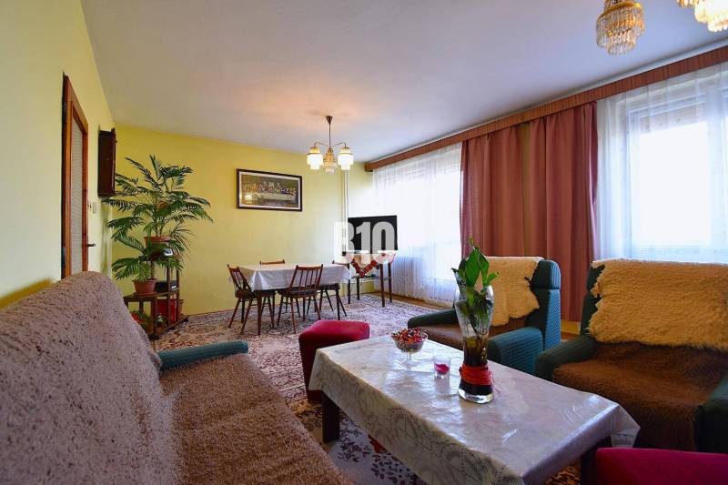 5 izbový  rodinný dom vo Varíne - Obývacia izba v rodinnom dome s kvetmi, kobercami a nábytkom.