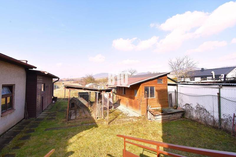 5 izbový  rodinný dom vo Varíne - Záhrada pri rodinnom dome v Žiline s drevenou prístavbou a výhľadom na krajinu.