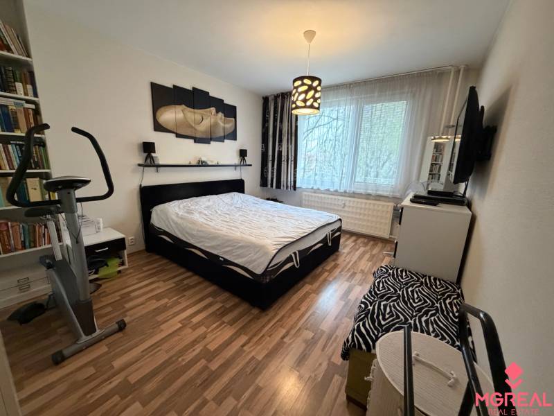 3 izbový byt  Topoľčany blízko centra - Spálňa v 3-izbovom byte s podlahou s dreveným dekorom a cvičebným bicyklom.