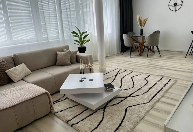 - PRENÁJOM - 2 IZBOVÝ BYT - DOLNÁ UL. - STARÉ MESTO - Svetlá obývačka s pohovkou, konferenčným stolíkom, jedálenským stolom a podlahou s dreveným dekorom.