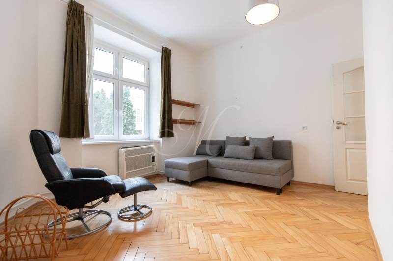 Priestranný 4-izbový byt s predzáhradkou, Staré Mesto - Svetlá obývacia izba s podlahou s dreveným dekorom v 4-izbovom byte, sivá sedačka, kreslo.