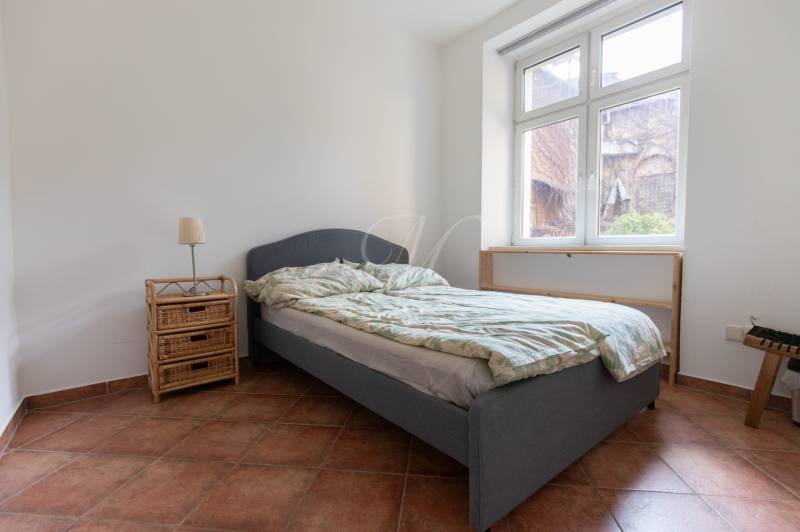 Priestranný 4-izbový byt s predzáhradkou, Staré Mesto - Spálňa v 4-izbovom byte s posteľou, nočným stolíkom a veľkým oknom.