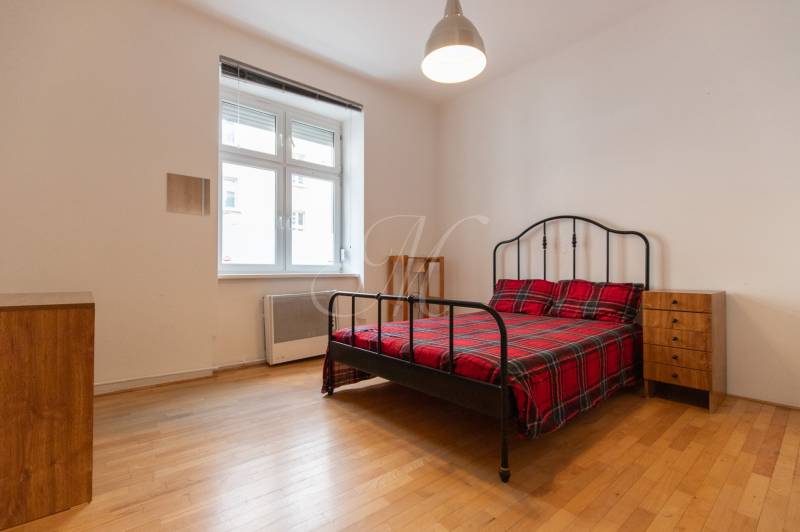 Priestranný 4-izbový byt s predzáhradkou, Staré Mesto - Spálňa v 4-izbovom byte s posteľou, nočnými stolíkmi a podlahou s dreveným dekorom.