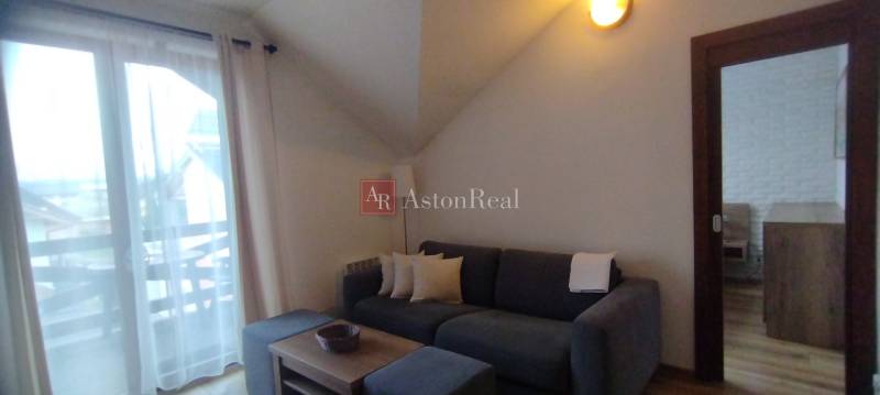 Predaj !Elegantný byt s wellness prvkami pri Jasnej - Obývacia izba v 2-izbovom byte s pohovkou, kávovým stolom a presklenými dverami na balkón.