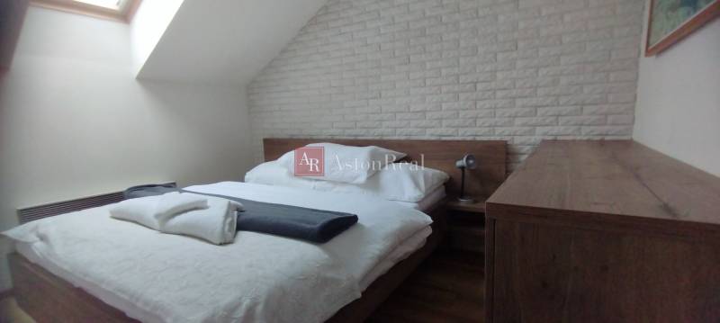 Predaj !Elegantný byt s wellness prvkami pri Jasnej - Spálňa v 2-izbovom byte s posteľou, lampou a tehlovým obkladom na stene.