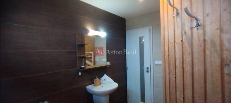 Predaj !Elegantný byt s wellness prvkami pri Jasnej - Kúpeľňa v 2-izbovom byte s tmavými obkladmi, zrkadlom a bielou umývadlovou skrinkou.