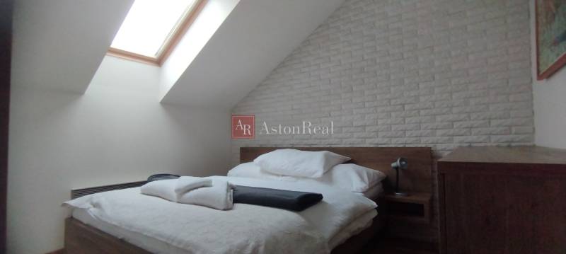 Predaj !Elegantný byt s wellness prvkami pri Jasnej - Spálňa v 2-izbovom byte s posteľou, strešným oknom a tehlovým obkladom.