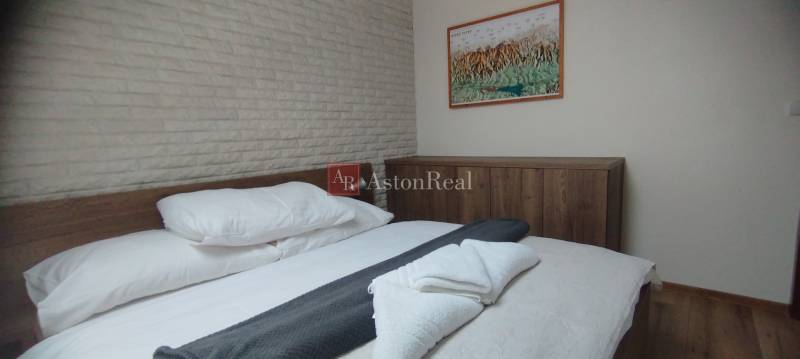 Predaj !Elegantný byt s wellness prvkami pri Jasnej - Spálňa v 2-izbovom byte s posteľou a skriňou, podlaha s dreveným dekorom.