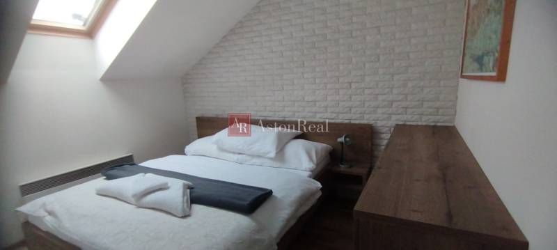 Predaj !Elegantný byt s wellness prvkami pri Jasnej - Spálňa s posteľou a strešným oknom v 2-izbovom byte s dekoratívnym tehlovým obkladom.