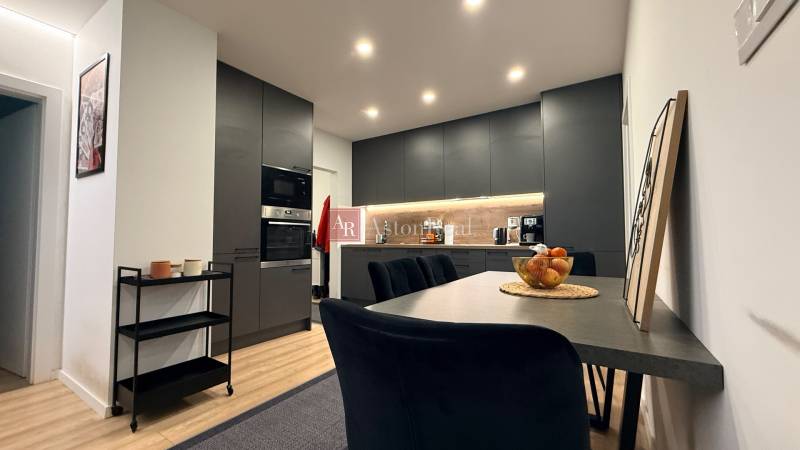 KOMPLETNE prerobený 4i byt s balkónom, 77m2 - ZÁTVOR - Kuchyňa v 4-izbovom byte s podlahou s dreveným dekorom, čiernymi skriňami a jedálenským stolom.