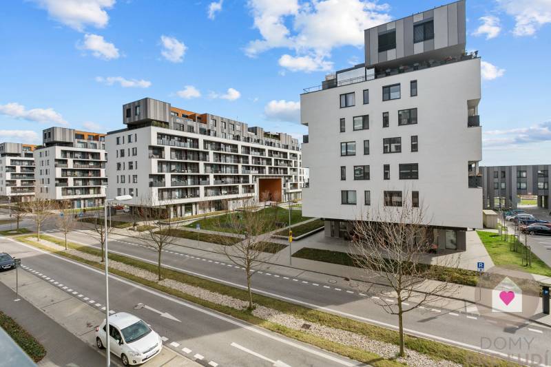 BA/PETRŽALKA-Prenájom 1i bytu s klimatizáciou a balkónom - Slnečnice - Petržalka: Biele obytné budovy s parkovacími miestami na ulici a modrou oblohou.
