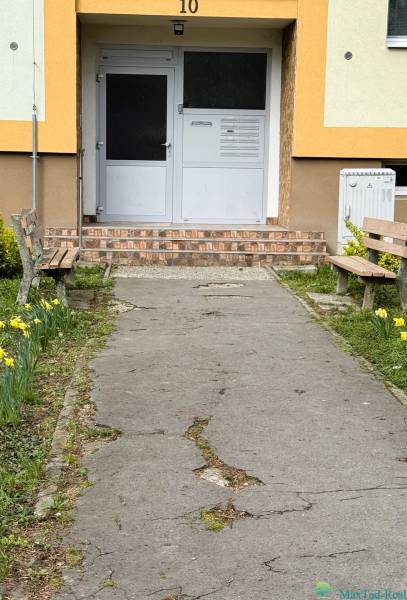 REZERVOVANÉ  3-izbový byt | Škultétyho ulica,  77,4 m², Trebišov. , - Vchod do budovy na Škultétyho ulici v Trebišove s lavičkami a záhonmi kvetov.