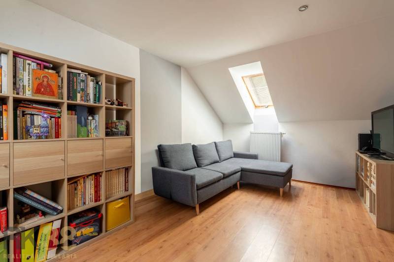 Predaj priestranného rodinného domu v historickej časti Popradu  - Obývacia izba s rohovou sedačkou, knihovňou a podlahou s dreveným dekorom v rodinnom dome.