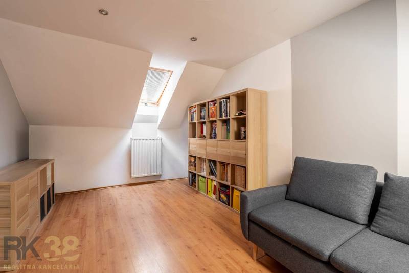 Predaj priestranného rodinného domu v historickej časti Popradu  - Podkrovná izba v rodinnom dome s podlahou s dreveným dekorom a pohodlnou sedačkou.