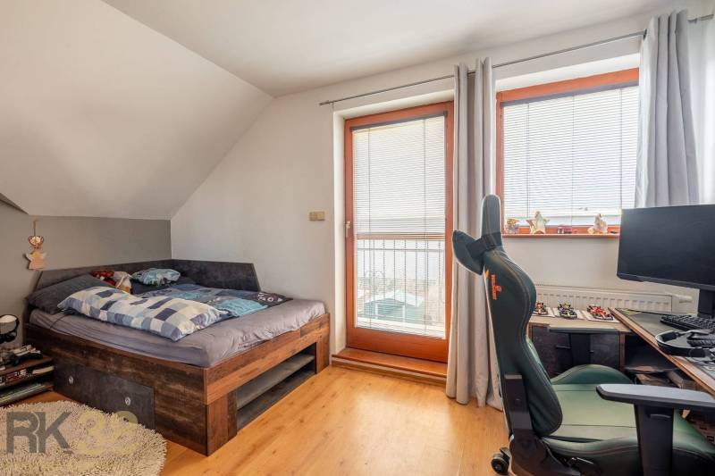 Predaj priestranného rodinného domu v historickej časti Popradu  - Izba s posteľou, pracovným stolom a stoličkou; podlaha s dreveným dekorom.