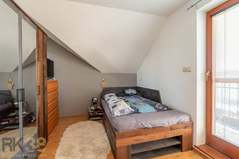 Predaj priestranného rodinného domu v historickej časti Popradu  - Spálňa v rodinnom dome s útulnou posteľou, šikmým stropom a podlahou s dreveným dekorom.