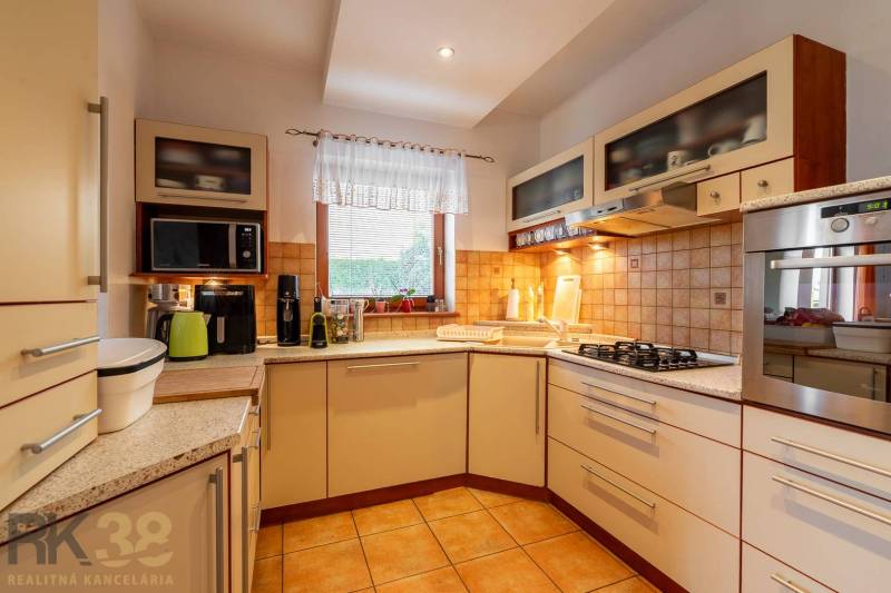 Predaj priestranného rodinného domu v historickej časti Popradu  - Kuchyňa v rodinnom dome so zabudovanými spotrebičmi, keramickým drezom a oknom.