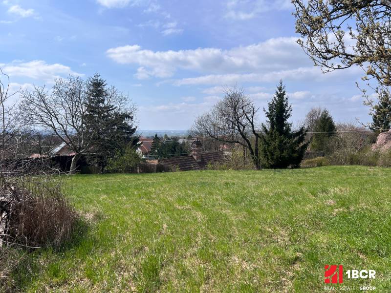 STAVEBNÝ POZEMOK S DUŠOU LEN PÁR MINÚT OD BRATISLAVY V OBCI MARIANKA - Zeleň na pozemkoch - bývanie v Marianke na Budovateľskej ulici obklopená stromami a neďalekými domami.