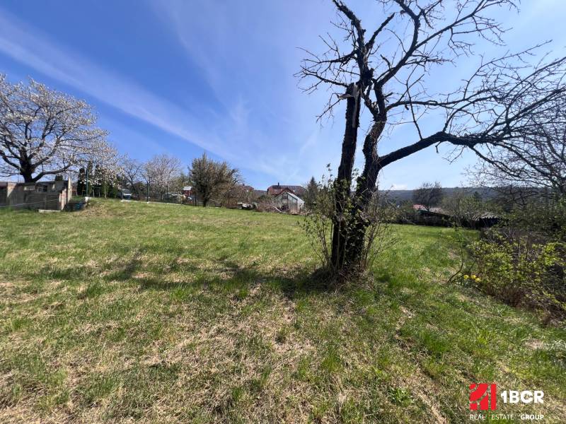 STAVEBNÝ POZEMOK S DUŠOU LEN PÁR MINÚT OD BRATISLAVY V OBCI MARIANKA - Pozemky - bývanie na Budovateľskej ulici v Marianke s trávnatou plochou a stromami.