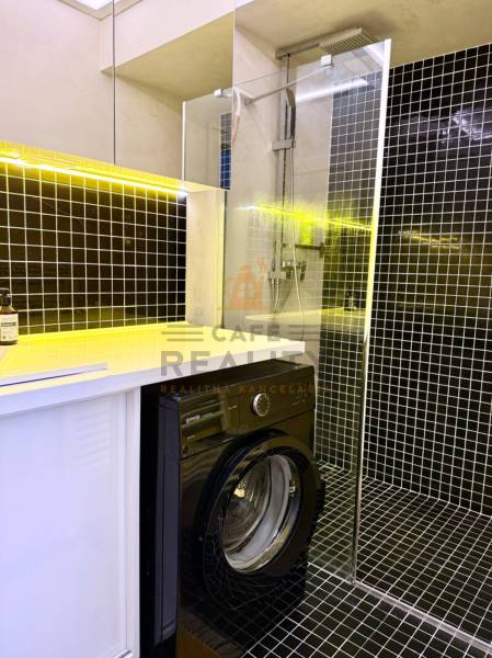 Na prenájom 2 izbový byt, Bratislava, Staré Mesto, Wilsonova ulica - Kúpeľňa v 2-izbovom byte s práčkou, sprchovým kútom a žltým osvetlením nad umývadlom.