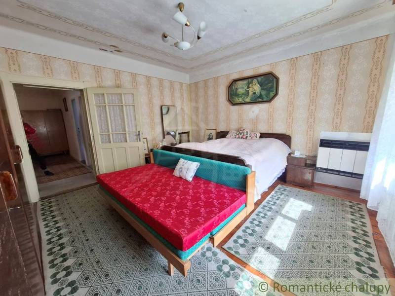 Pôvodný priestranný rodinný dom na rozľahlom pozemku v malebnej obci Ľ - Spálňa v rodinnom dome s dvojposteľou, gaučom a vzorovanými kobercami.