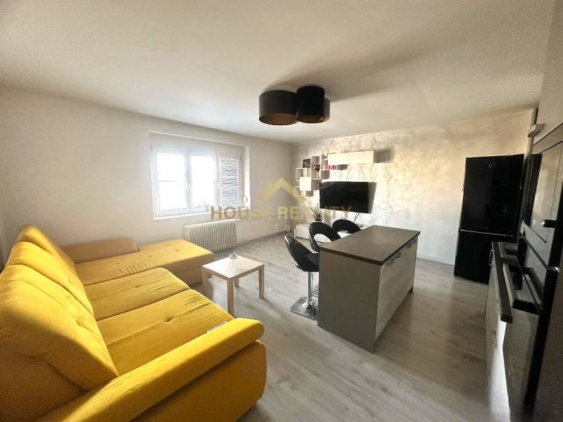 Prenájom pekný 2 izbový byt Šancová ulica, Bratislava III. Nové Mesto - Obývacia izba s veľkou žltou sedačkou, kuchynským ostrovom a televíziou v 2-izbovom byte.