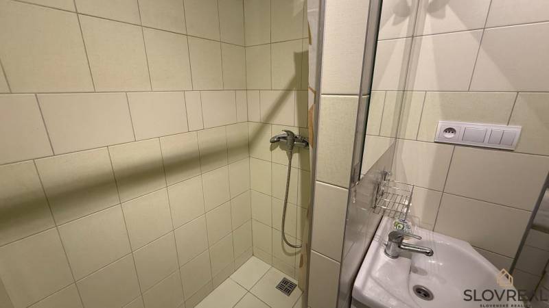 1-izbový byt na prenájom v Hliníku nad Hronom - Kúpeľňa v 1-izbovom byte so sprchovým kútom a umývadlom, obložená bielymi dlaždicami.