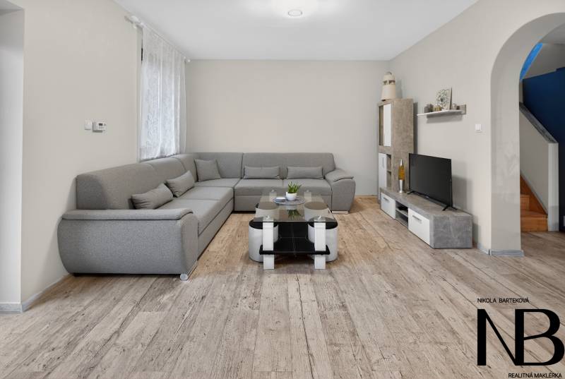 Rodinný dom s veľkým pozemkom a priestorom na podnikanie – T.Jastrabie - Obývacia izba v rodinnom dome s podlahou s dreveným dekorom a sivou sedačkou.