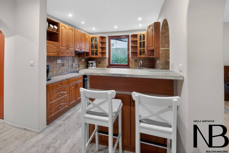 Rodinný dom s veľkým pozemkom a priestorom na podnikanie – T.Jastrabie - Kuchyňa v rodinnom dome s barovým pultom, drevenými skrinkami a podlahou s dreveným dekorom.