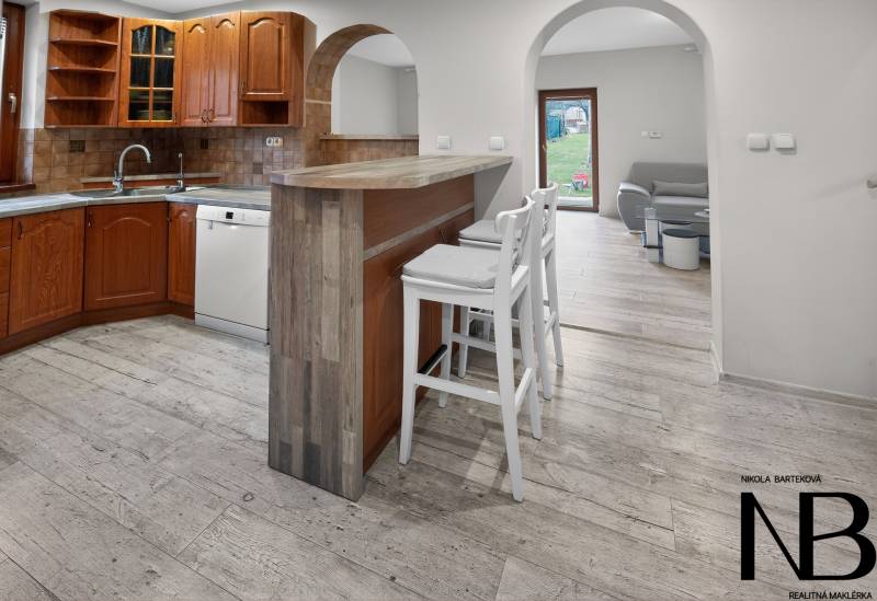Rodinný dom s veľkým pozemkom a priestorom na podnikanie – T.Jastrabie - Kuchyňa v rodinnom dome s barovým pultom, bielymi stoličkami a podlahou s dreveným dekorom.