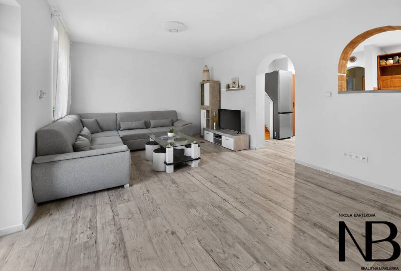 Rodinný dom s veľkým pozemkom a priestorom na podnikanie – T.Jastrabie - Obývacia izba v rodinnom dome s pohodlnou sivou sedačkou a podlahou s dreveným dekorom.