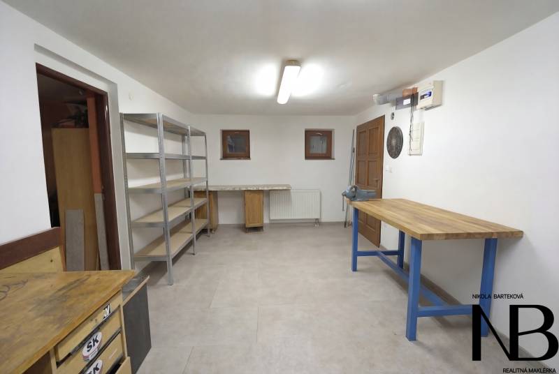 Rodinný dom s veľkým pozemkom a priestorom na podnikanie – T.Jastrabie - Dielňa s pracovnými stolmi a regálovými policami v rodinnom dome.