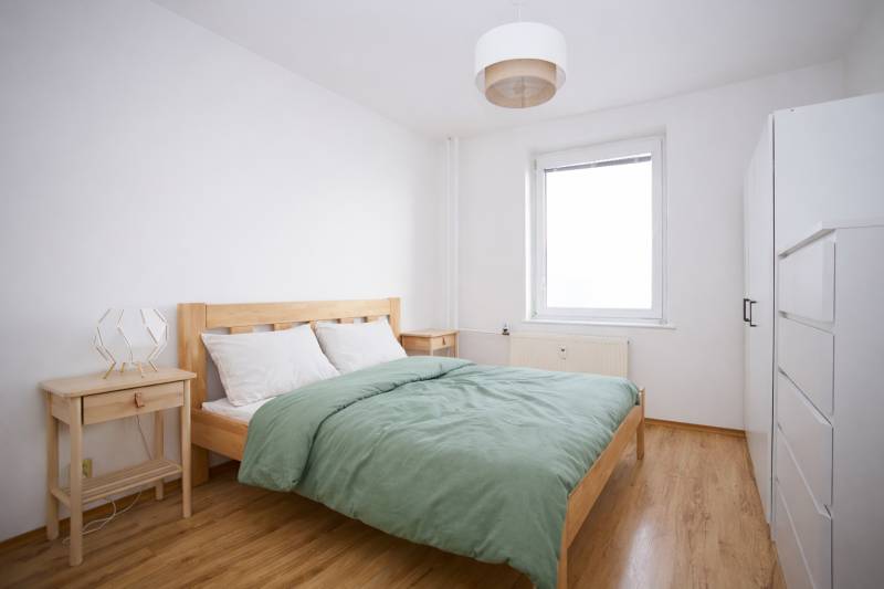 NA PREDAJ-3-izbový byt s loggiou a výhľadom na centrum mesta, KE-JUH - Spálňa v 3-izbovom byte s posteľou, nočnými stolíkmi a podlahou s dreveným dekorom.