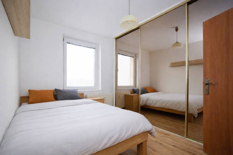 NA PREDAJ-3-izbový byt s loggiou a výhľadom na centrum mesta, KE-JUH - Spálňa v 3-izbovom byte s podlahou s dreveným dekorom a veľkým zrkadlovým šatníkom.