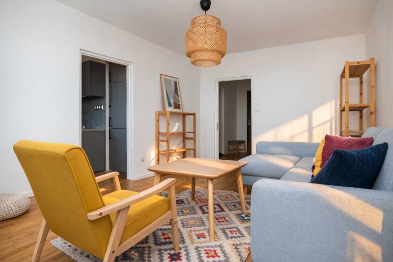 NA PREDAJ-3-izbový byt s loggiou a výhľadom na centrum mesta, KE-JUH - Obývacia izba v 3-izbovom byte s dreveným dekorom, sivou sedačkou a žltým kreslom.