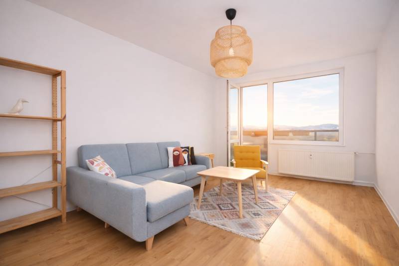 NA PREDAJ-3-izbový byt s loggiou a výhľadom na centrum mesta, KE-JUH - Obývacia izba 3-izbového bytu s pohovkou, kreslom a podlahou s dreveným dekorom.