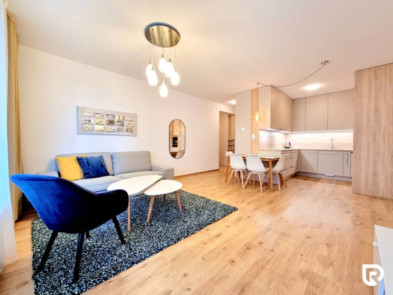 REZERVOVANÉ I Posledný investičný krásny 2-izbový byt | 62 m² | - Obývacia izba v 2-izbovom byte s kuchynským kútom a podlahou s dreveným dekorom.