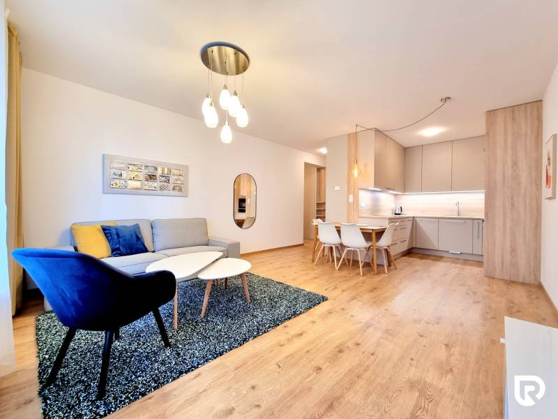 REZERVOVANÉ I Posledný investičný krásny 2-izbový byt | 62 m² | - Obývacia izba 2-izbového bytu s pohovkou, kreslom, kuchynským kútom a podlahou s dreveným dekorom.
