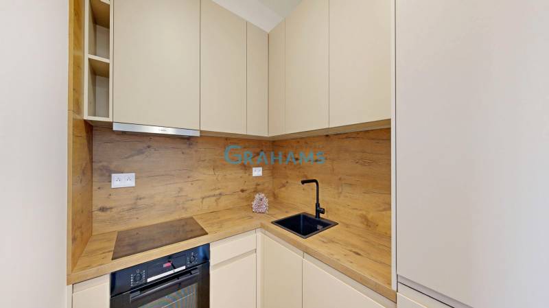 Nový, ešte neobývaný 1,5-izbový byt, parkovanie, Metropolis, Bottova - Kuchyňa v 2-izbovom byte s dreveným dekorom, úložné skrinky a spotrebiče.