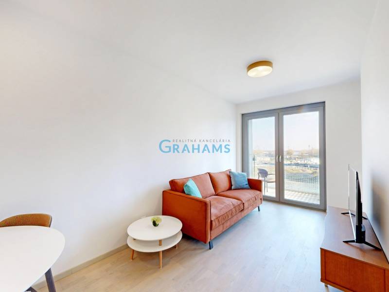 Nový, ešte neobývaný 1,5-izbový byt, parkovanie, Metropolis, Bottova - Obývacia izba v 2-izbovom byte s oranžovou pohovkou, TV a balkónovými dverami.