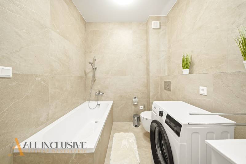 Na prenájom 2-izb. byt s terasou, Dun. Streda -Florida - Kúpeľňa so svetlými obkladmi, vaňou, práčkou a dekoratívnymi rastlinami v 4-izbovom byte.