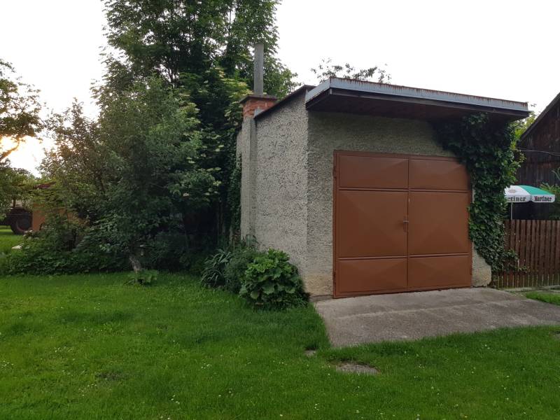PREDAJ – Rodinný dom s druhou samostatnou stavbou, garážou  - Garáž v rodinnom dome na ulici v Blatnici, obklopená zeleňou a popínavými rastlinami.