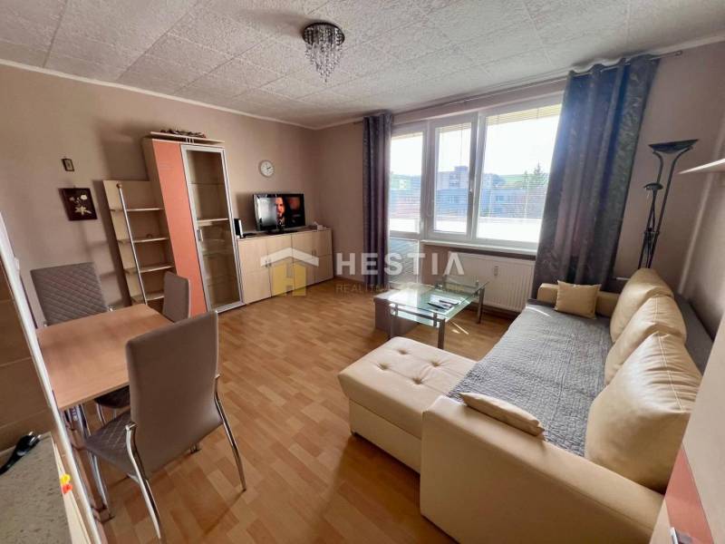 Prenájom 2‑izbového kompletne zariadeného bytu v Brezovej pod Bradlom - Obývacia izba v 2-izbovom byte s podlahou s dreveným dekorom, béžová sedačka, jedálenský stôl.