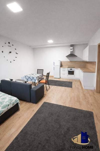 Moderný 2-izbový byt v centre Kežmarku na predaj - Kuchyňa s pohovkou v 2-izbovom byte s podlahou s dreveným dekorom a nástennými hodinami.