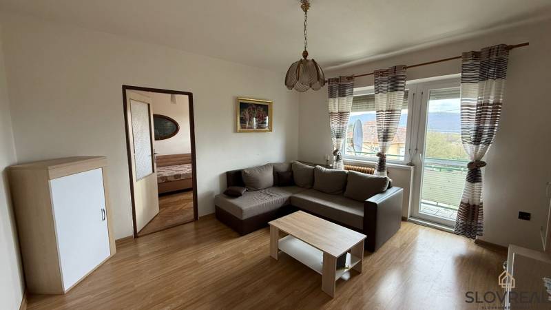 Na predaj 3i byt Pukanec - Obývacia izba v 3-izbovom byte so sedačkou a podlahou s dreveným dekorom.