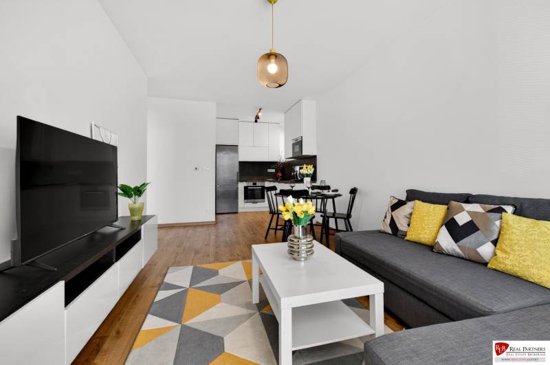 Predaj 2-izbový byt GREEN VILLAGE, 51m2, loggia, Dunajská Lužná - Obývacia izba v 2-izbovom byte s pohovkou, stolíkom a podlahou s dreveným dekorom.